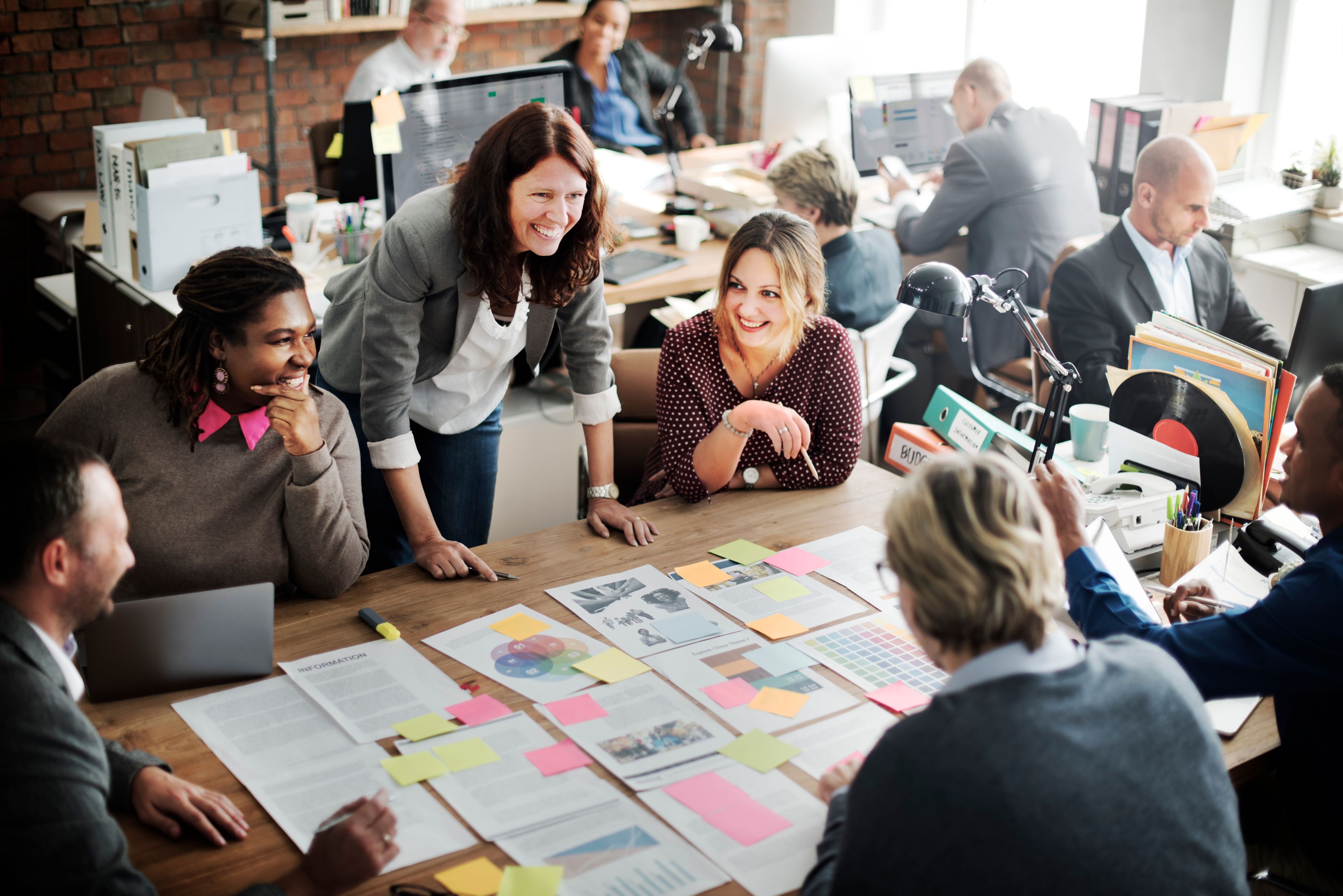 several people smile as they work on organizing papers on a shared desk